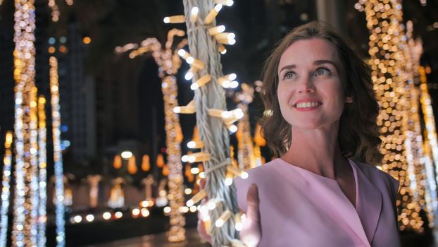 The girl gently touches the glowing lights on a palm tree in the night city of Dubai