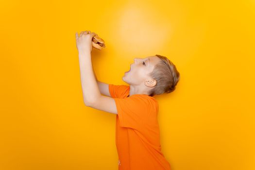 a boy in an orange T-shirt stands sideways and holds a hamburger he wants to eat