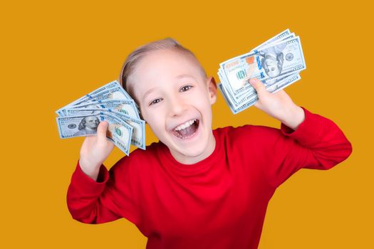 a cheerful child in red holds a bunch of dollar bills in front of his face