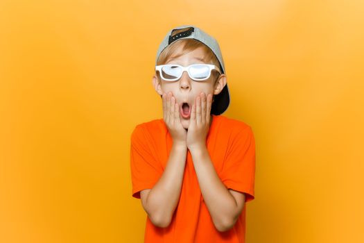 a child in glasses for watching movies opened his mouth in surprise and holds his cheeks with his hands