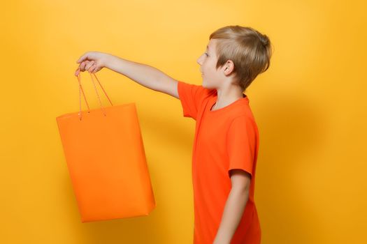 the boy stretched out his hand to the side in which he holds an orange shopping bag
