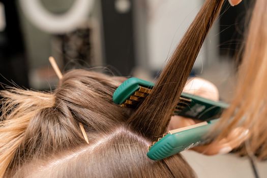 The hairdresser prepares a woman, makes a hairstyle with curls using a curling iron. Long light brown natural hair. Self care concept