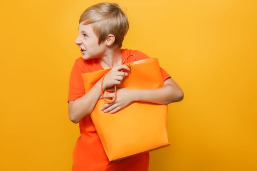 a boy in an orange T-shirt holds a package with both hands clutching it to his chest and is angry