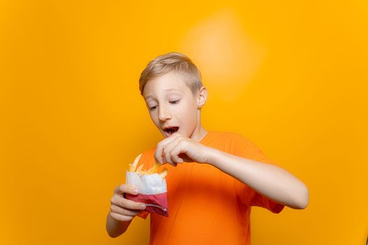 a boy in an orange T-shirt holds a bag of deep-fried potatoes in front of him and takes one piece out of it