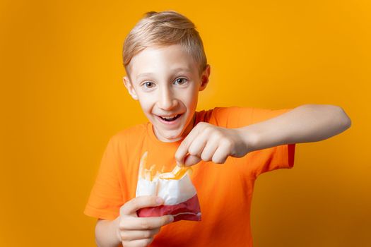 a boy in an orange T-shirt holds a bag of deep-fried potatoes in front of him