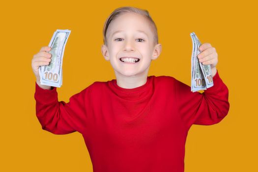 a cheerful child in red holds a bundle of dollar bills in front of him and makes funny faces