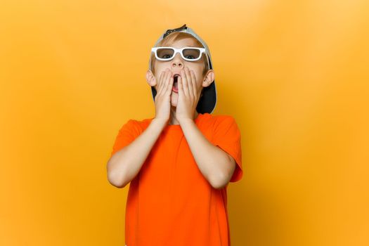 a child with glasses for watching movies covers his mouth with his hands he is very scared