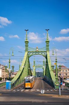 Scene at the crossroads of the embankment. A tram is traveling across an old bridge over the river. Budapest, Hungary - 08.25.2022