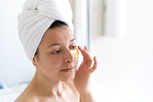 After a shower, the girl is wrapped in a towel and wears cosmetic patches for the skin under the eyes. Cosmetic procedures at home.