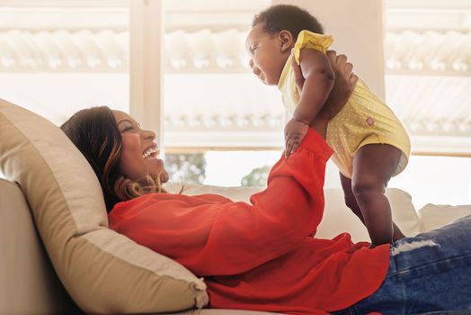 Being mother is the most fun I ever had. a mother holding up her baby while lying on her sofa at home