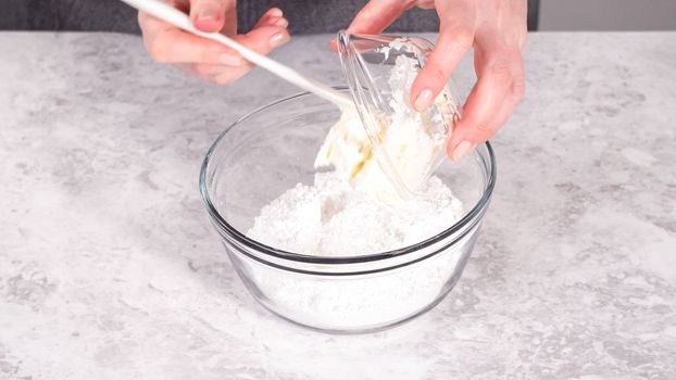 Step by step. Mixing ingredients in a glass mixing bowl to prepare cream cheese frosting.