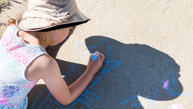 Little girl drawing with chalk on a sidewalk on the summer day.