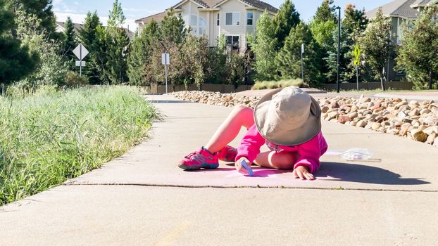 Little girl drawing with chalk on a sidewalk on the summer day.