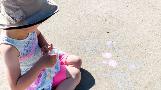 Little girl drawing with chalk on a sidewalk on the summer day.