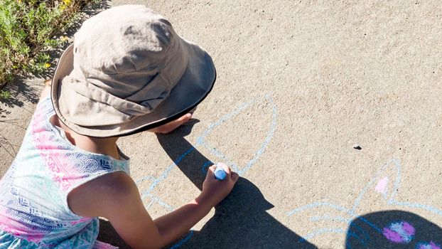 Little girl drawing with chalk on a sidewalk on the summer day.