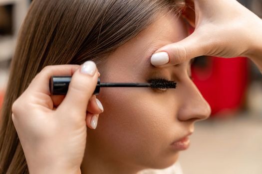 Makeup artist paints eyelashes to a woman in a beauty salon