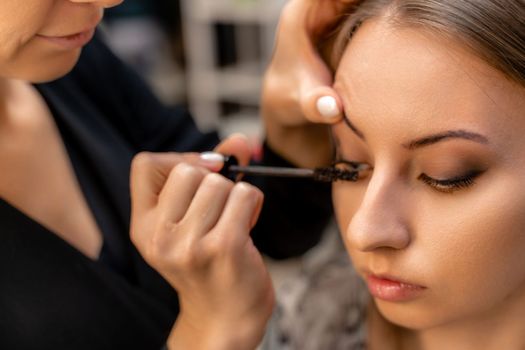 Makeup artist paints eyelashes to a woman in a beauty salon