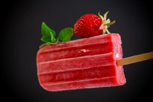cooked homemade strawberry ice cream on a stick, isolated on black background