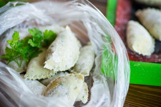 Raw green dough dumplings with parsley, dill. Raw dumplings in a bag on a wooden table.