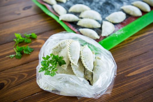 Raw green dough dumplings with parsley, dill. Raw dumplings in a bag on a wooden table.