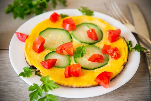 Fried omelet with zucchini, tomatoes, herbs in a plate on a wooden table.