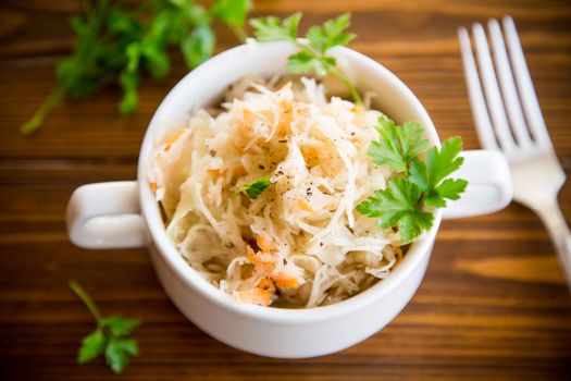 sauerkraut with carrots and spices in a bowl on a wooden table.