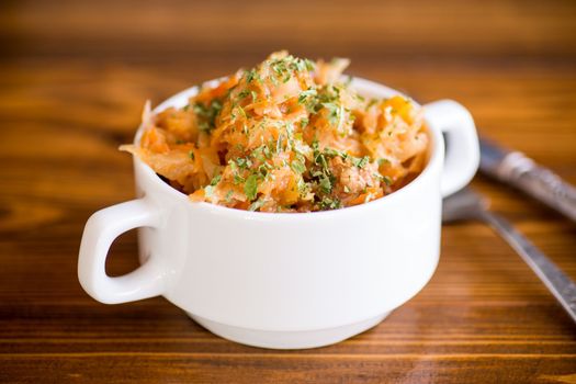 stewed cabbage with carrots and spices in a bowl on a wooden table.