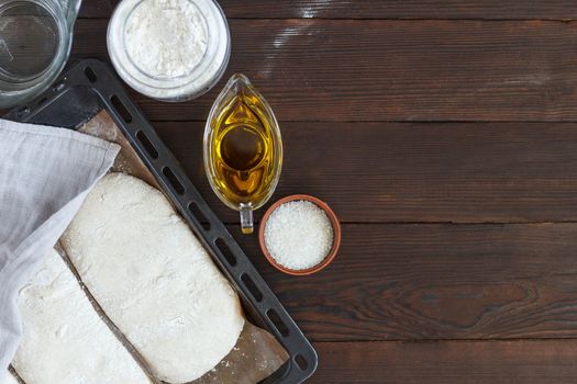 fresh raw dough for baking bread on a baking sheet, ready for baking with ingredients: flour, olive oil, water, salt on a wooden background.