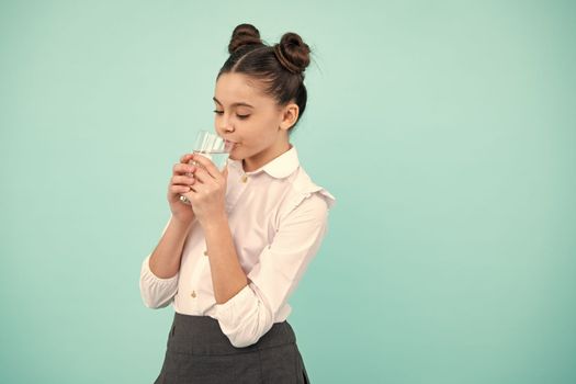 Teenage girl drinking water from glass on blue background. Daily life health. Drink water for health care and body balance. Thirsty child, dehydration