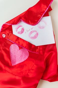 The inscription I love you on a white envelope with a print of lips made with red lipstick on a background of small red hearts and a red shirt. Valentine concept, vertical photo