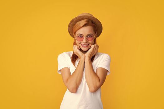 Smiling portrait of pretty young woman wearing sunglasses and straw hat over yellow background. Happy girl enjoying summer