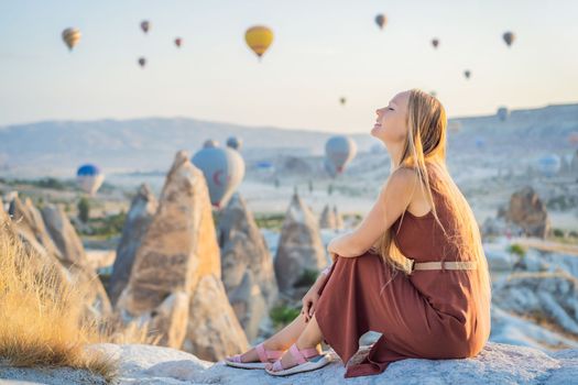 Tourist woman looking at hot air balloons in Cappadocia, Turkey. Happy Travel in Turkey concept. Woman on a mountain top enjoying wonderful view.