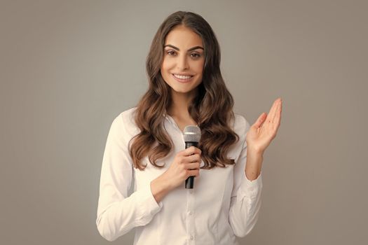 Woman speech, business woman holding a microphone. Happy smiling business woman holding mic, standing with microphone against grey background, wearing shirt