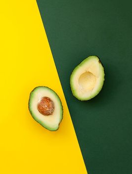 Organic avocado with seed, avocado halves and whole fruits on yellow and green background.
