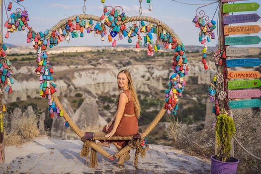 Young woman exploring valley with rock formations and fairy caves near Goreme in Cappadocia Turkey. Wish tree. Small multi-colored jugs with inscriptions, wishes hanging on the branches of a tree., against the backdrop of sand ruins and blue sky.