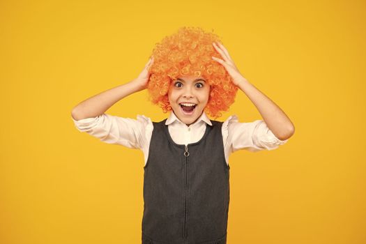 Funny kid in curly redhead wig. Time to have fun. Teen girl with orange hair, being a clown. Excited face, cheerful emotions of teenager girl