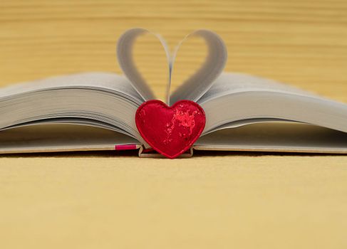 Valentine's Day concept. red heart on the background of an open book. Heart from folded sheets. Yellow background. Heart symbol. Close-up. soft focus.