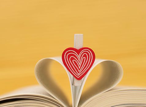 Valentine's Day concept. red heart on the background of an open book. Heart from folded sheets. Yellow background. Heart symbol. Close-up. soft focus.