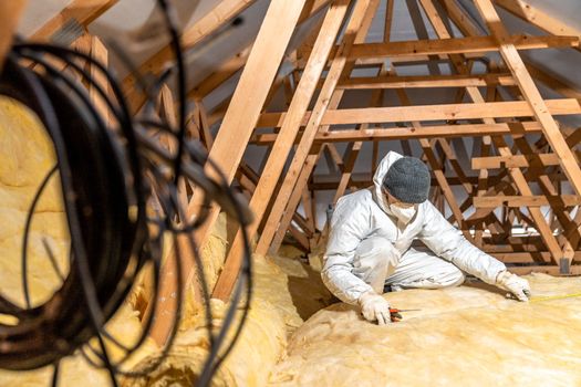 a man insulates the roof and ceiling of the house with glass wool