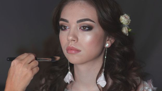 Girl make-up artist applies powder on the face of the model