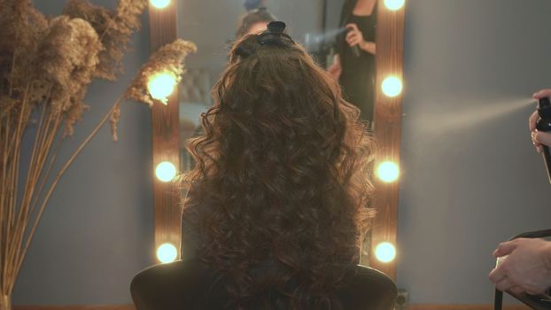 The hairdresser fixes curly hair with hairspray