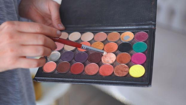 Makeup artist holds shadows in his hand and paints a model