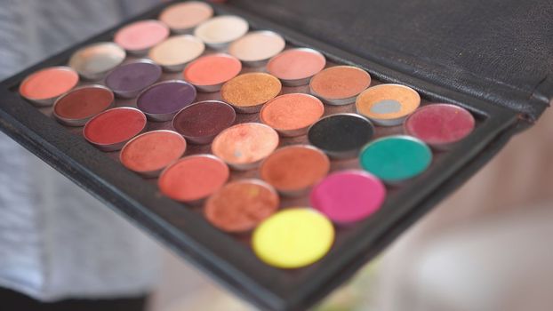 Makeup artist holds shadows in his hand and paints a model
