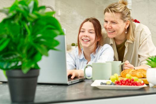 Happy mother and daughter having breakfast in kitchen and using digital devices. Lifestyle, Morning breakfast, mother and daughter together.