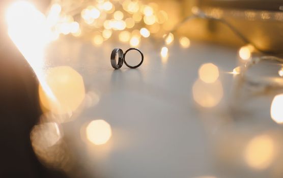 Wedding rings on blured bokeh glowing golden background. Symbol of love and romance on a textured glitter background with copy space for your greeting or congratulations.
