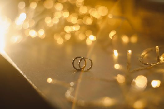 Wedding rings on blured bokeh glowing golden background. Symbol of love and romance on a textured glitter background with copy space for your greeting or congratulations.
