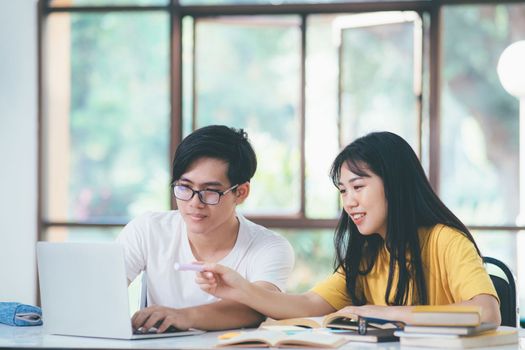 Young asian university students are studying for an exam. There are tutor books with friends. They are classmates that try to help each other. They have been tutoring for many hours in the campus.