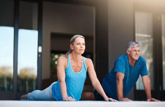 Starting off our day with a much needed yoga session. Full length shot of a mature and happy couple doing yoga exercises outside of their home