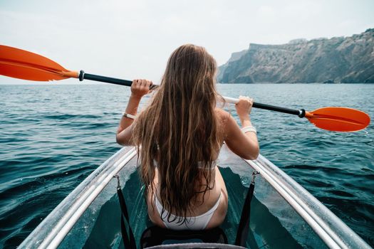 Woman in kayak back view. Happy young woman with long hair floating in transparent kayak on the crystal clear sea. Summer holiday vacation and cheerful female people having fun on the boat.