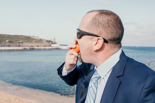 Male persimmon park. Hipster millennial man in a tie and jacket bites off a persimmon while sitting on a park bench in slow motion Young business people eat golden persimmons at lunchtime